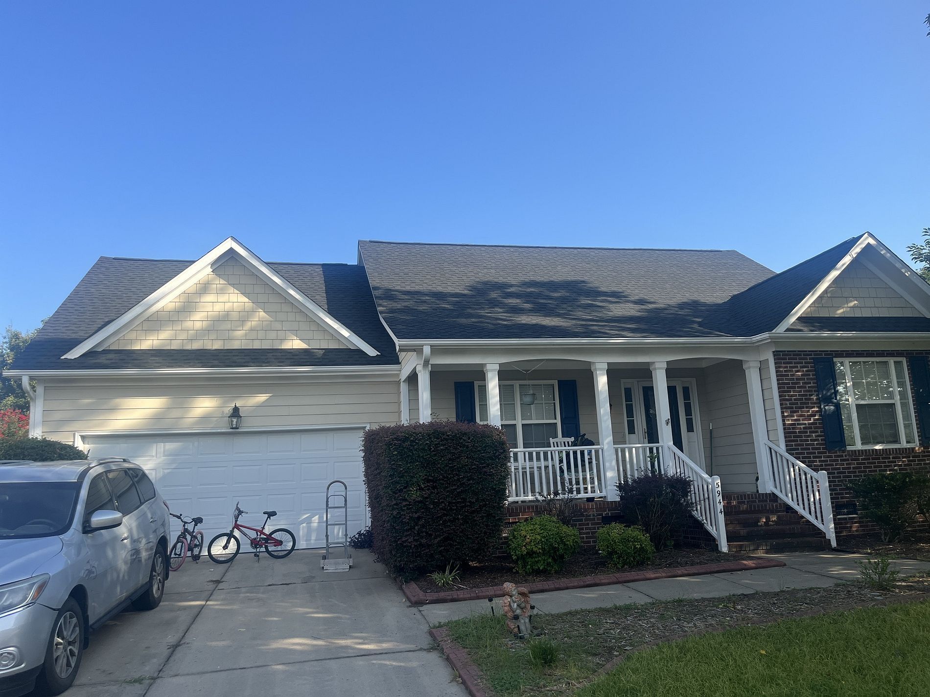 A one-story suburban house with a white garage, front porch, and shingled roof under a clear blue sky.