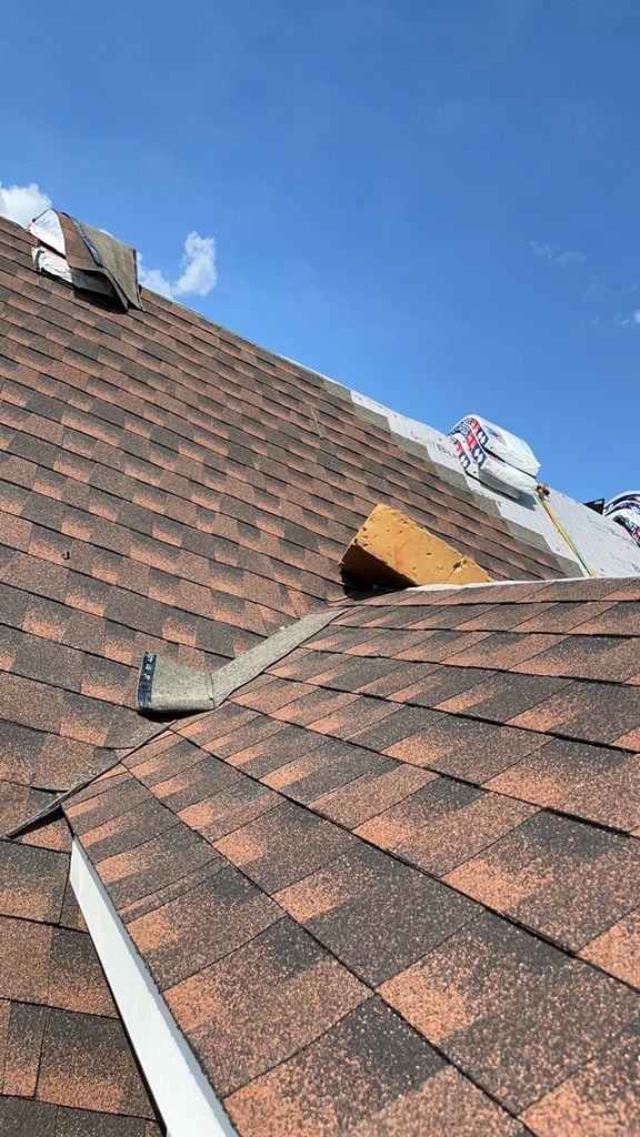 A damaged roof with missing shingles, exposed wood decking, and a vent under a bright blue sky.