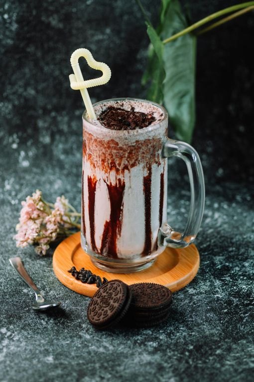 A milkshake with a heart shaped straw and oreo cookies on a table.