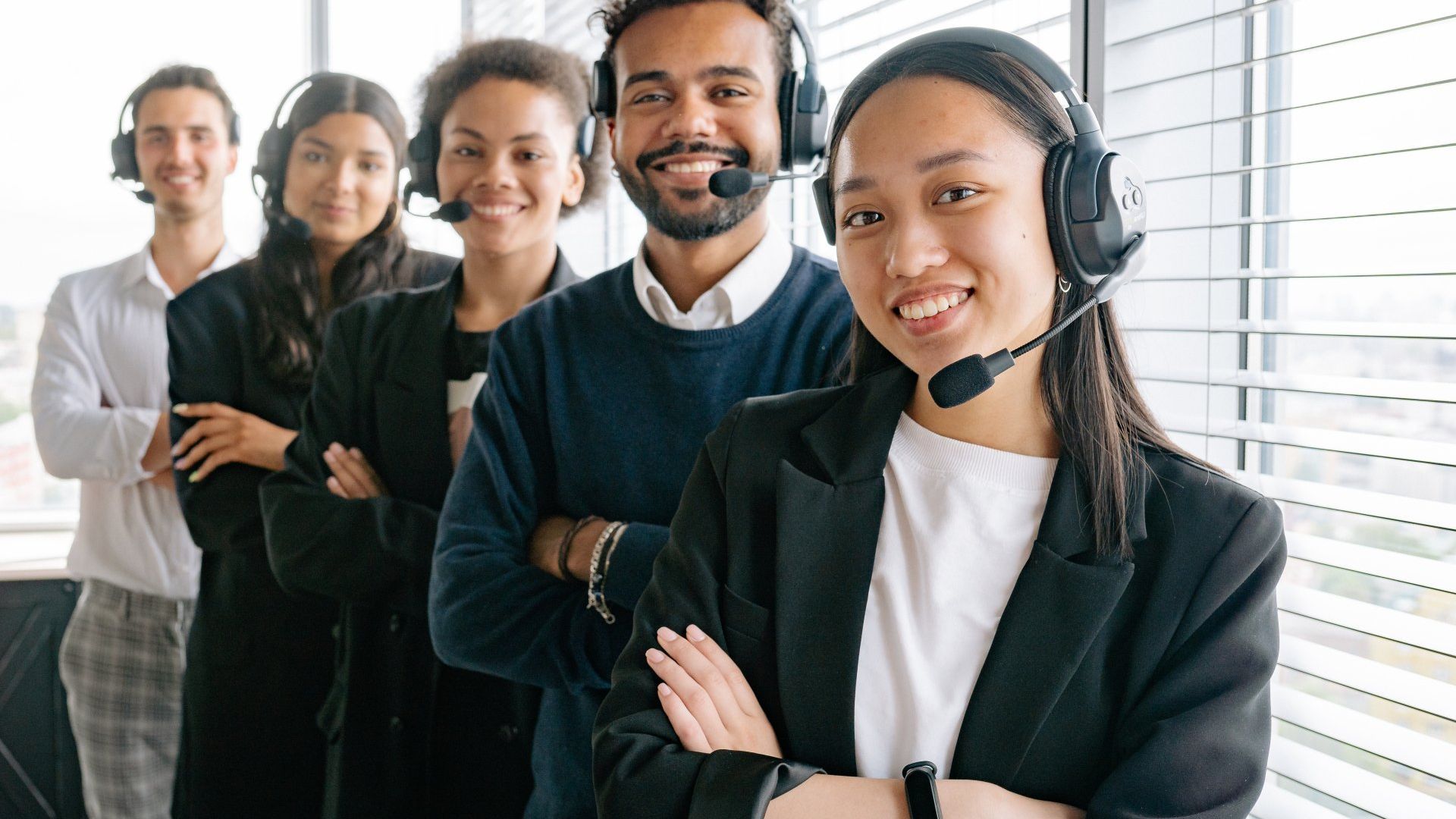 A group of people wearing headsets are standing next to each other in front of a window.