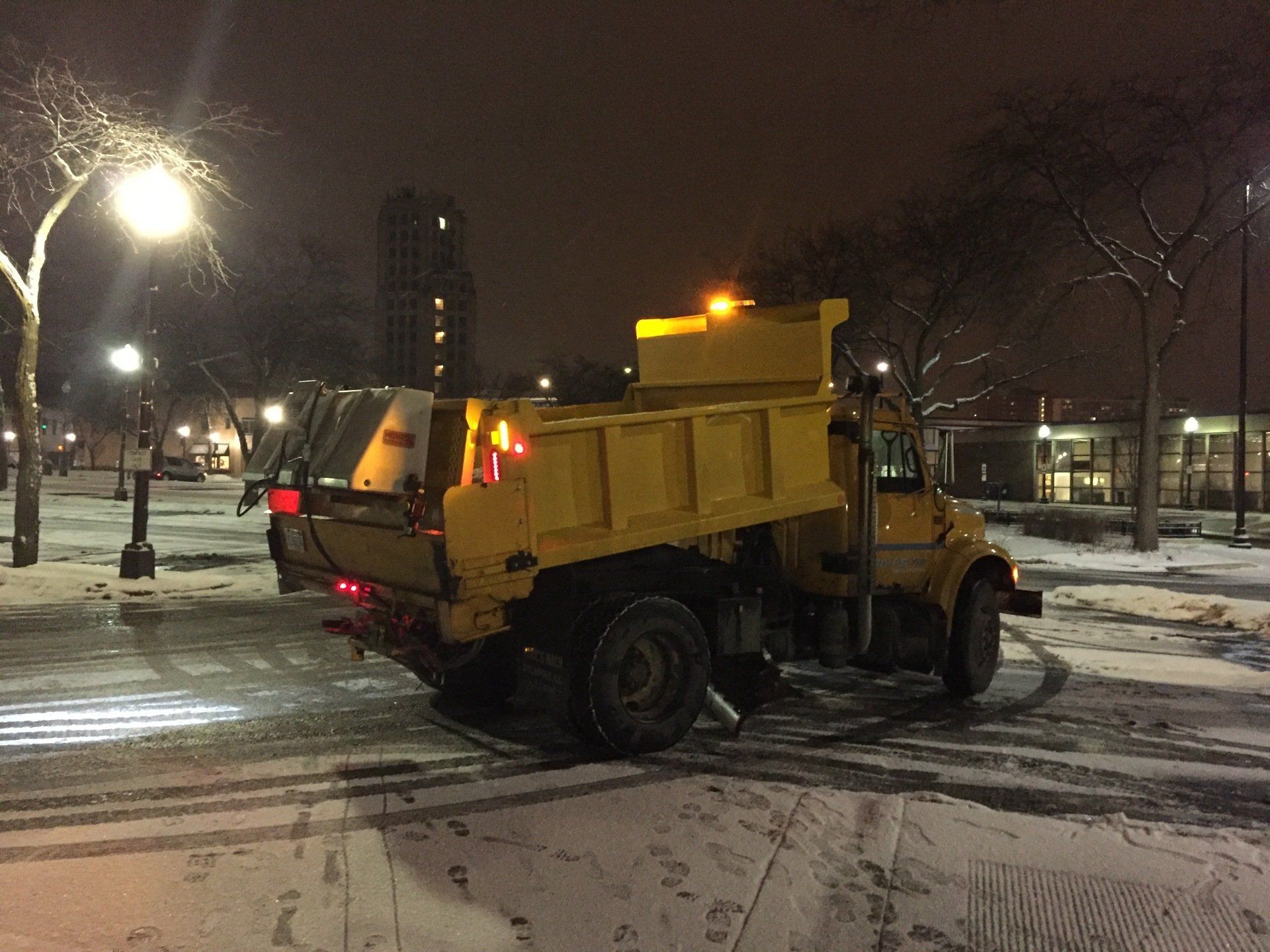 Yellow municipal snow plow truck salting icy parking lot at night in winter