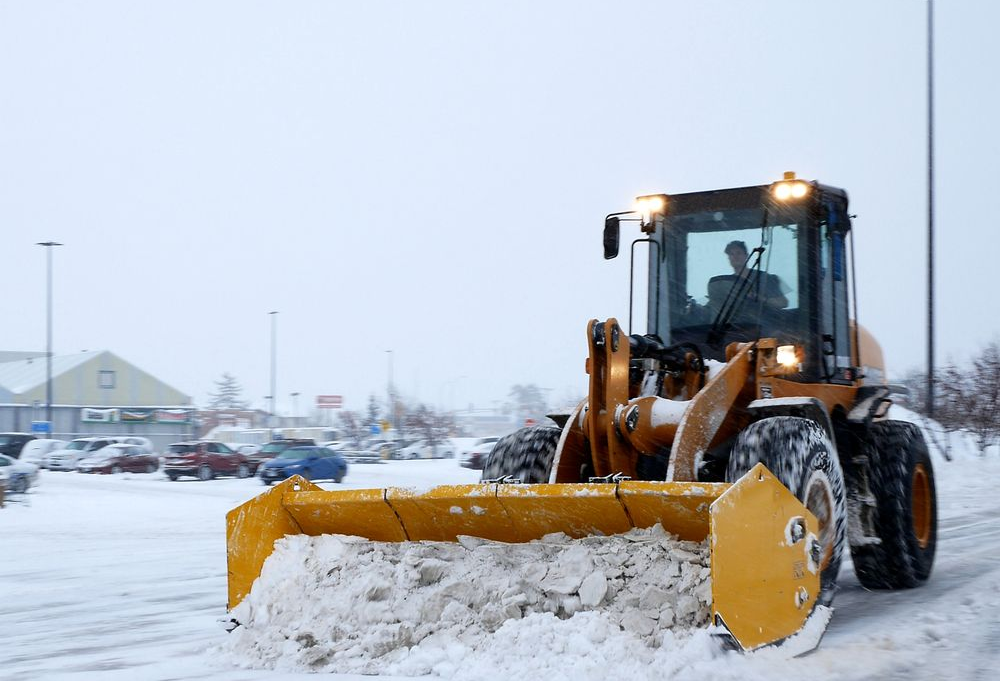 Yellow snowplow clearing snow in a parking lot on a snowy day