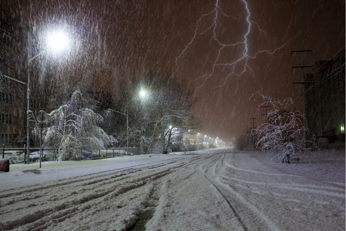 Lightning is strikes in the night sky over a snowy street.