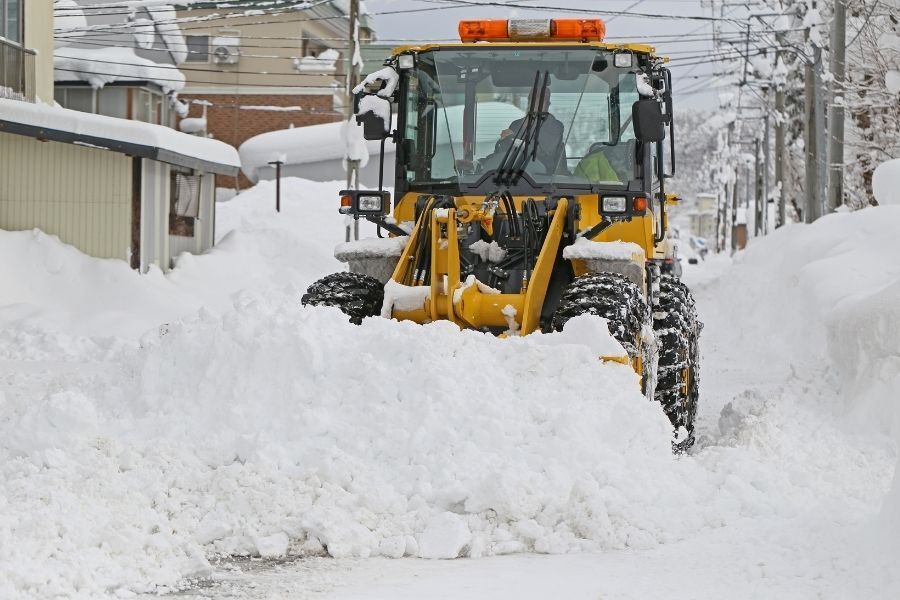 Front-end loader clearing deep snow from commercial roadway during winter storm