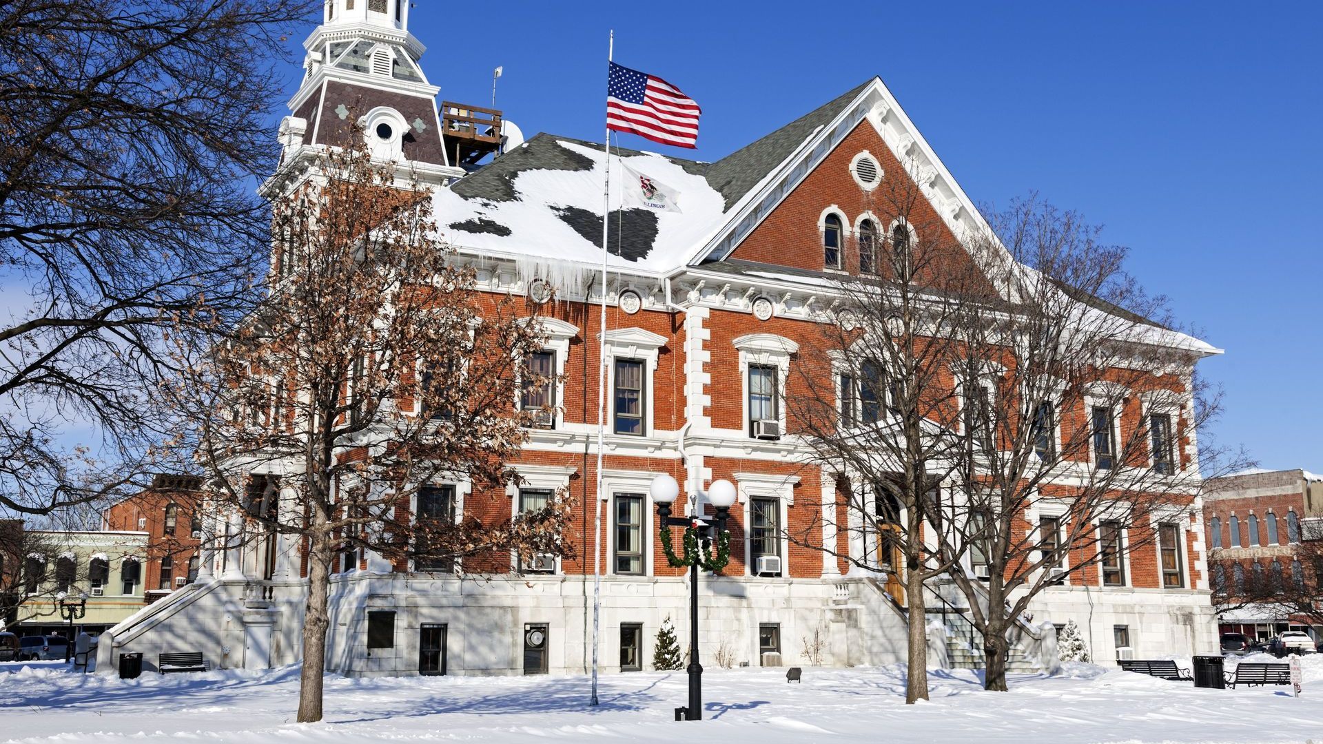 Historic red brick municipal building in Illinois with snow-covered roof and American flag in winter