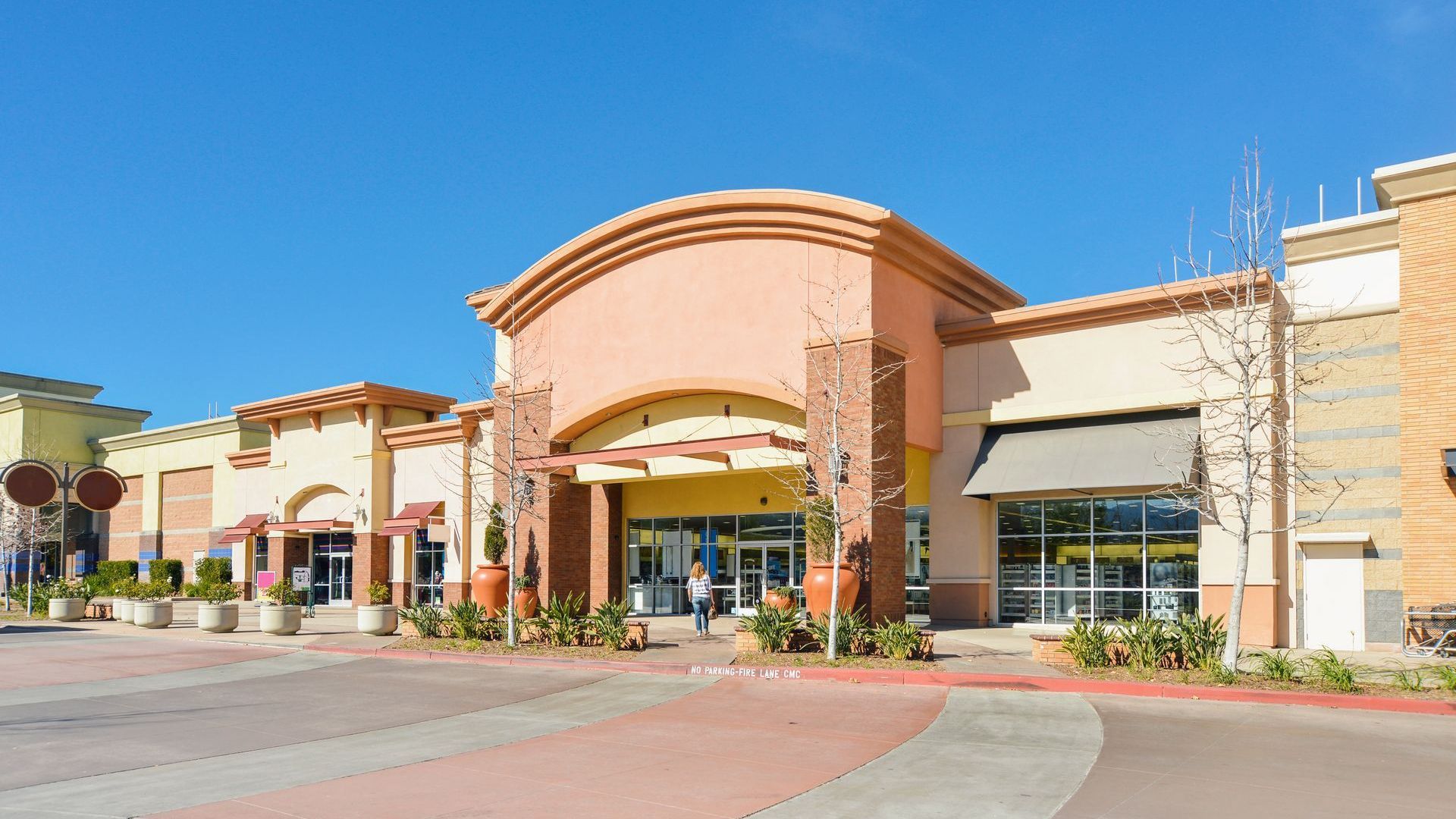 Large commercial retail shopping center entrance with storefronts and parking area