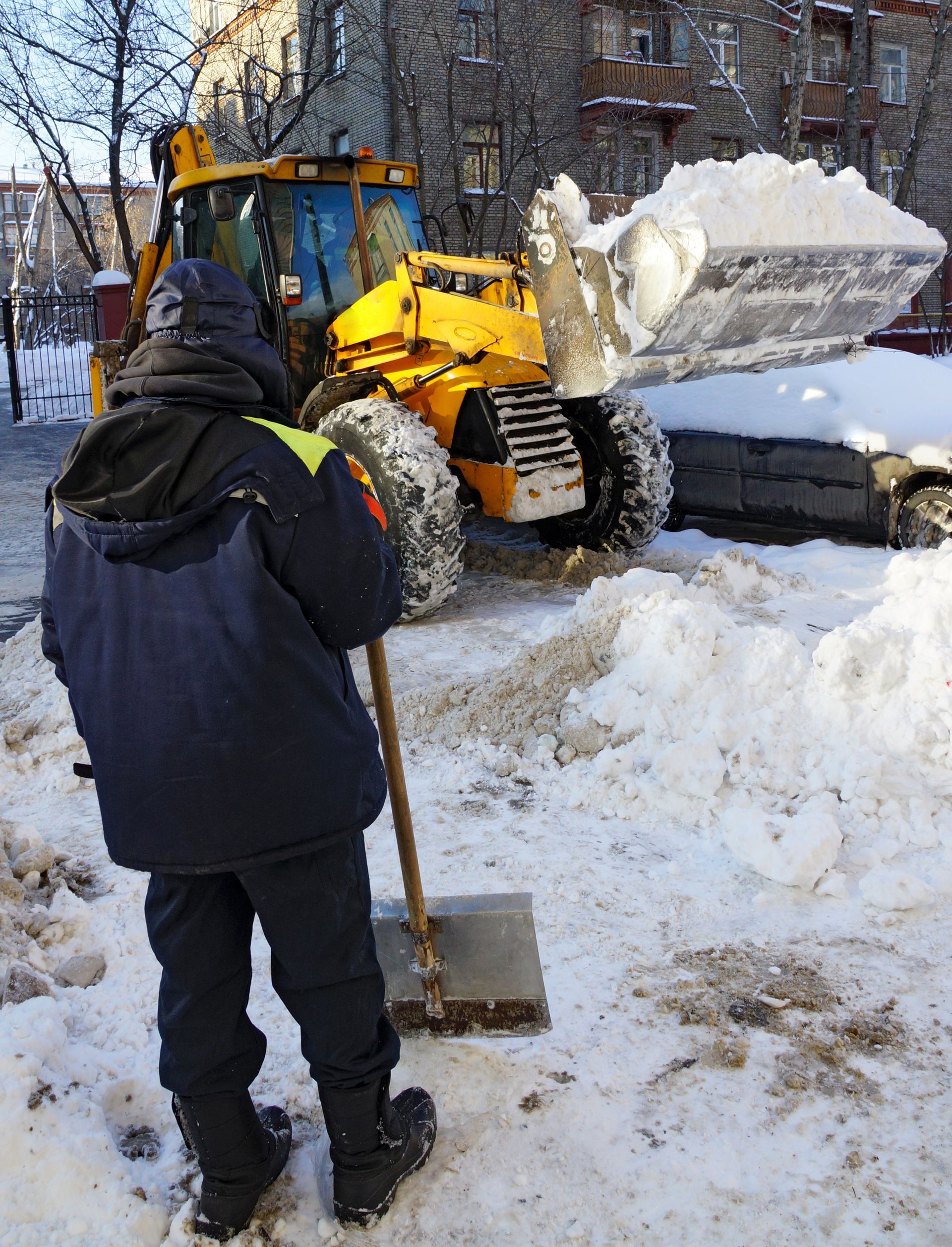 Snow removal crew clearing commercial property with loader and shovel during winter.