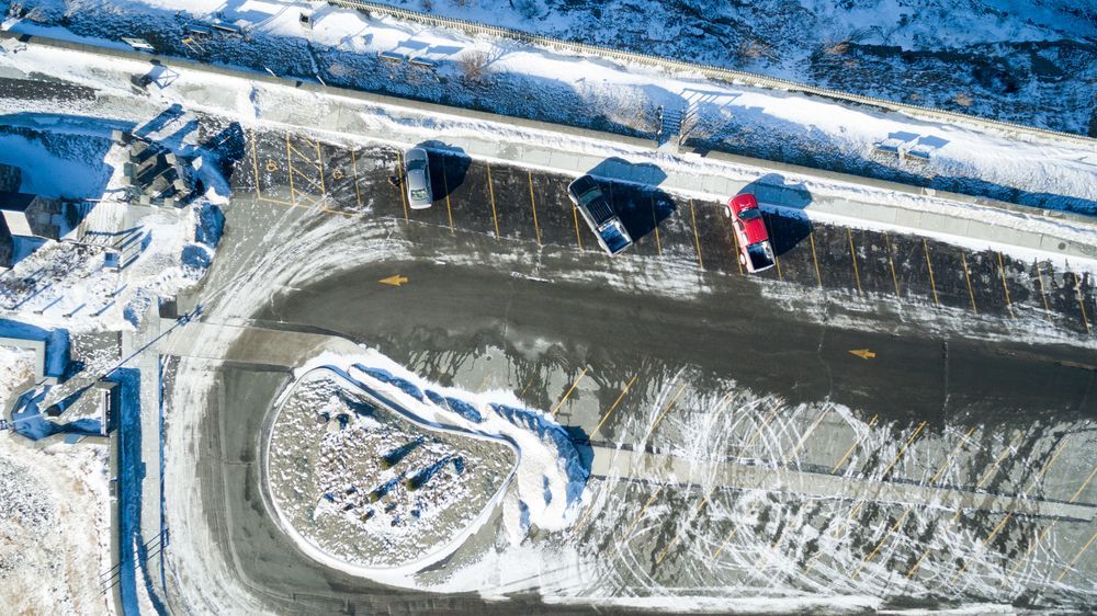 Aerial view of a snowy road with parked cars and a large roundabout covered in snow.