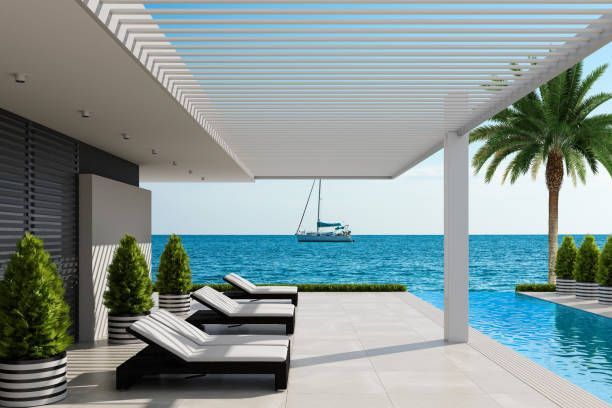Modern seaside patio with lounge chairs, palm tree, and sailboat on blue ocean