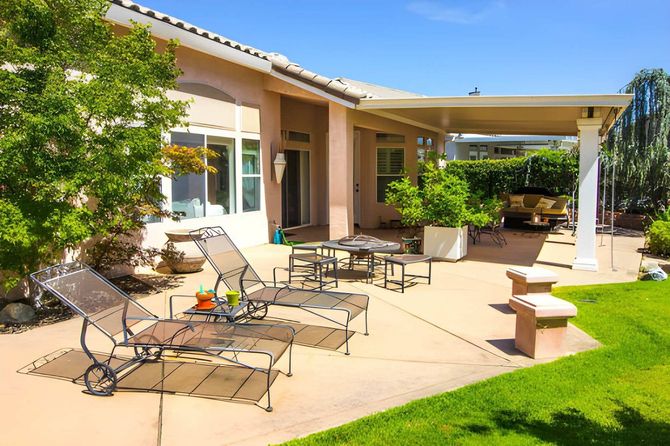 Sunny backyard patio with lounge chairs, outdoor table, and green lawn beside a house
