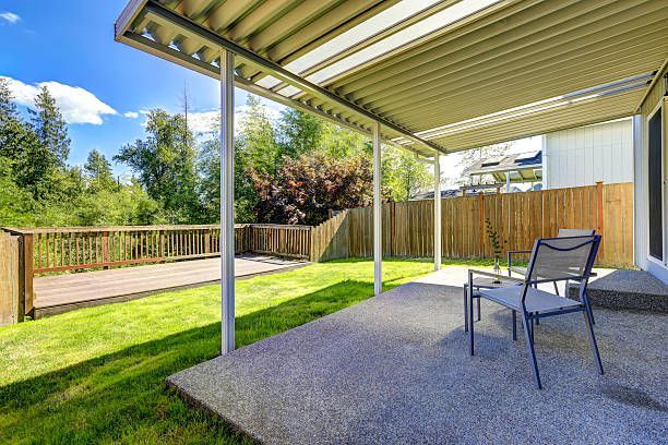Covered patio with two chairs overlooking a sunny backyard and wooden deck railing