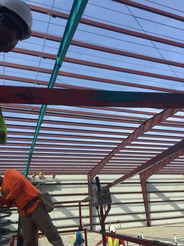 Workers installing a red metal roof frame at a construction site