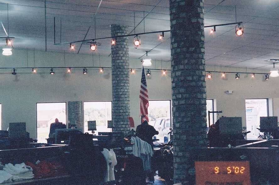 Dim indoor room with people at desks, hanging lights, brick pillars, and an American flag in the center.