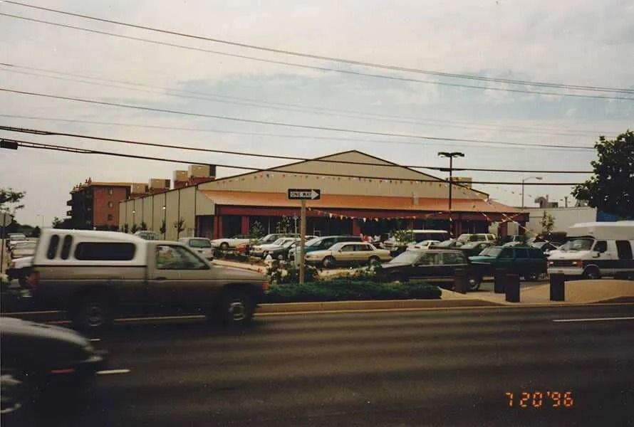 Parking lot outside a beige store with cars and a white pickup truck on a busy street