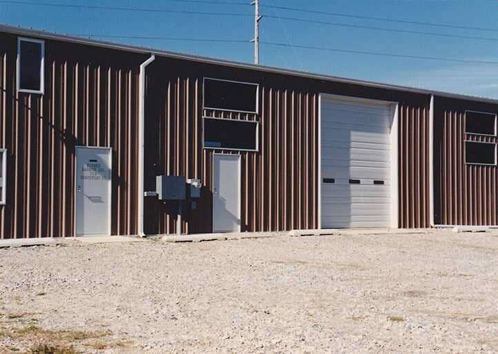 Brown metal building with several doors and windows on a gravel lot under a clear blue sky