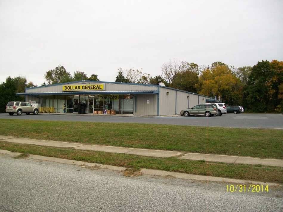Small roadside store with parked cars under a gray sky, surrounded by trees.