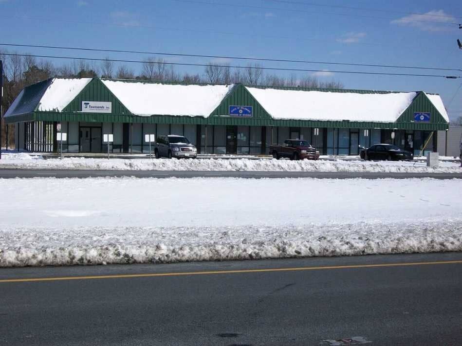 Snow-covered storefronts along a roadside under a clear blue sky