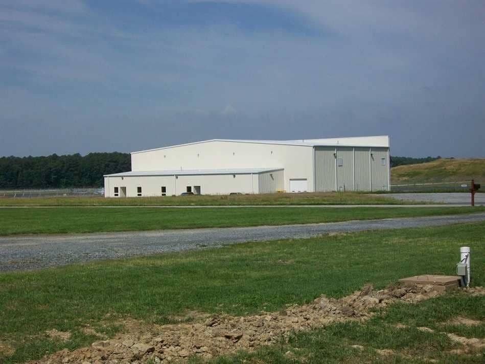 Large white industrial building on a grassy field under a cloudy sky
