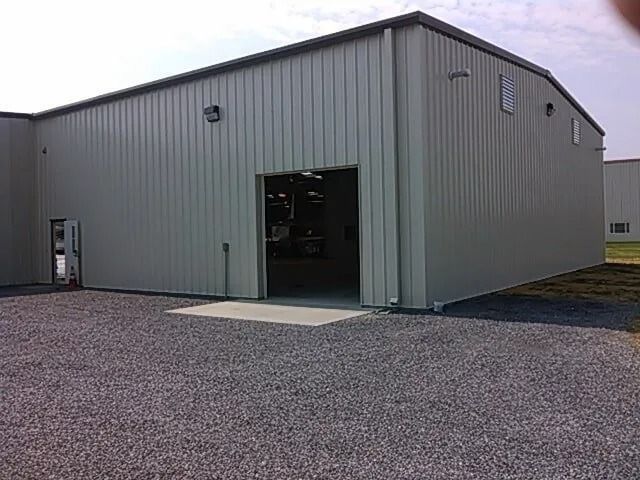 Large gray metal warehouse with open bay doors on a gravel lot