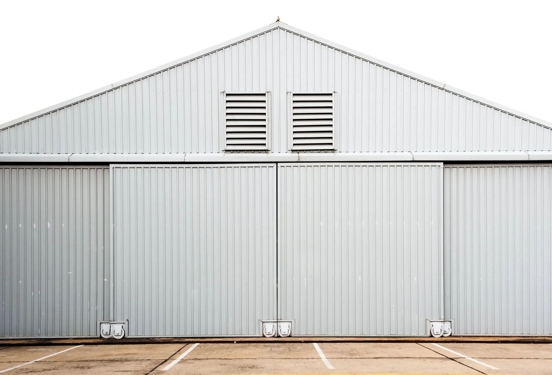 Gray corrugated metal building with a peaked roof and shuttered vents above closed doors