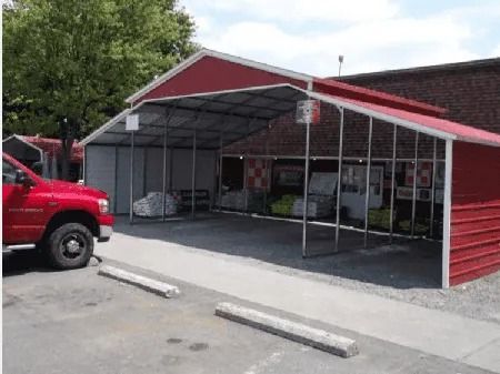 Red truck parked beside a red-roofed covered carport with white metal framing and concrete parking stops.
