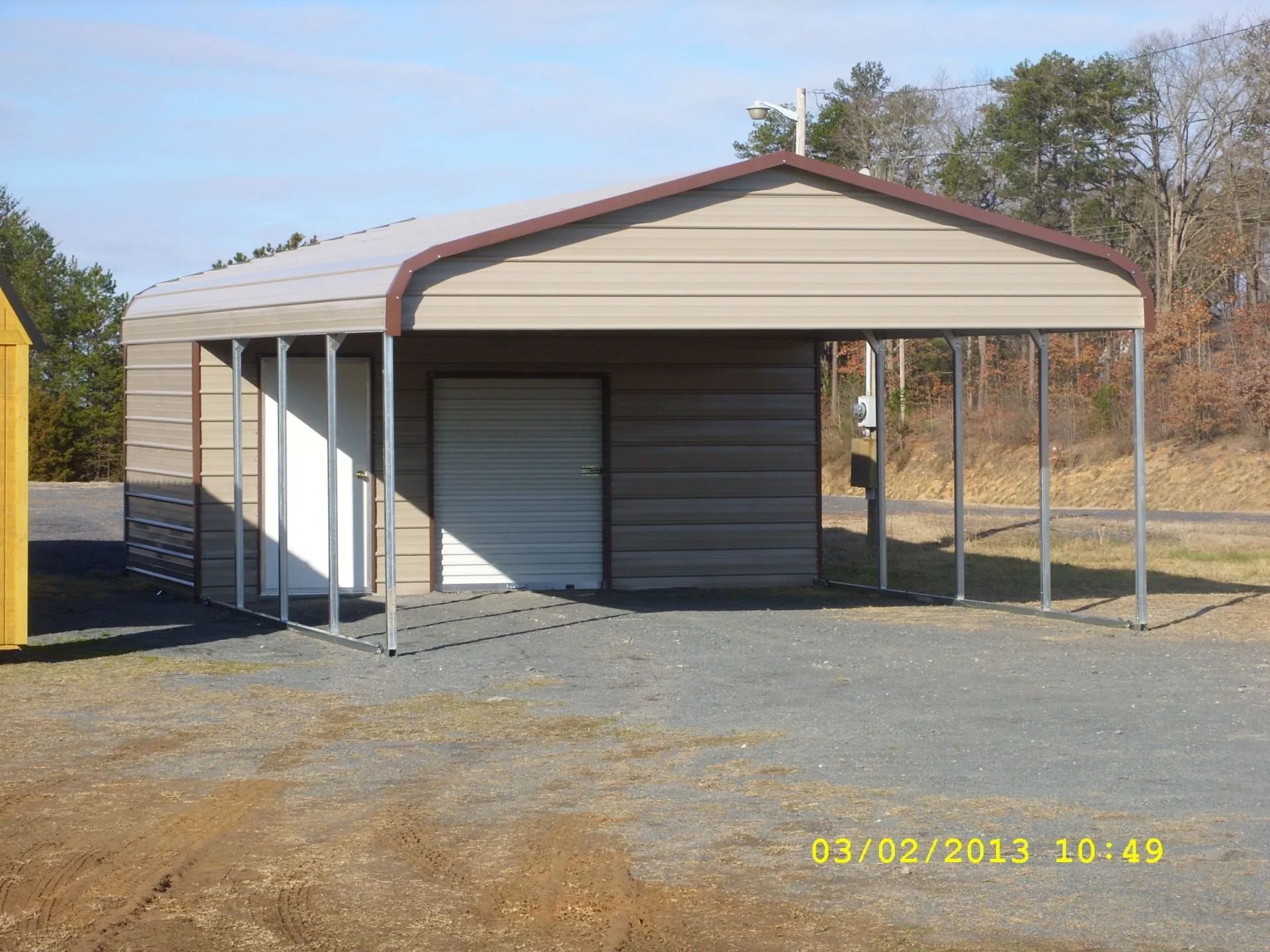 Metal carport with a white garage door and open sides on a gravel lot under a clear sky
