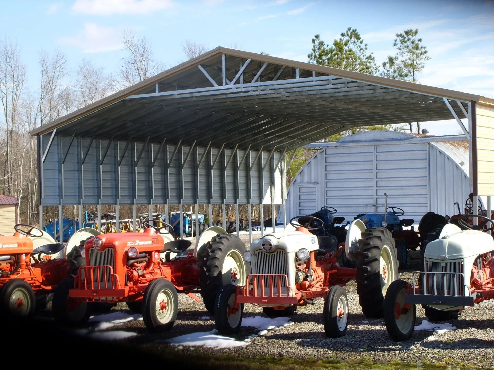 Row of vintage tractors parked under a large open-sided shed outdoors