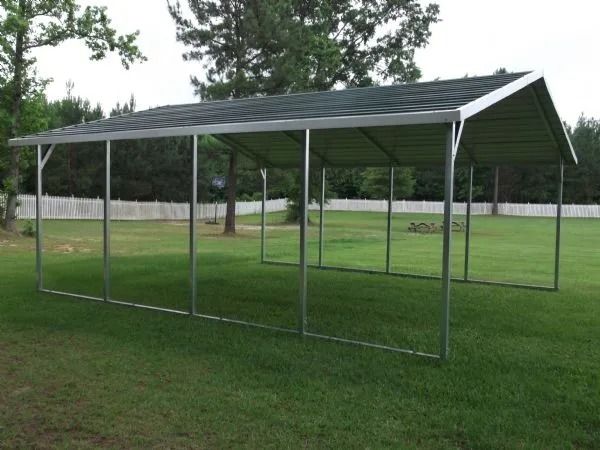 Long metal livestock shelter with a dark roof on a grassy field