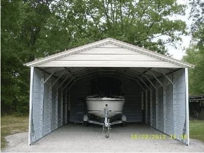 Boat stored in an open metal carport, with a white trailer centered inside and trees behind it.