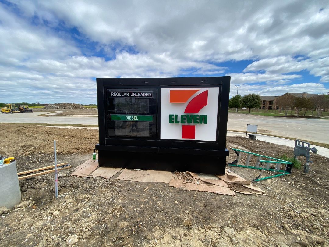 A 7 eleven sign is sitting in the middle of a dirt field.