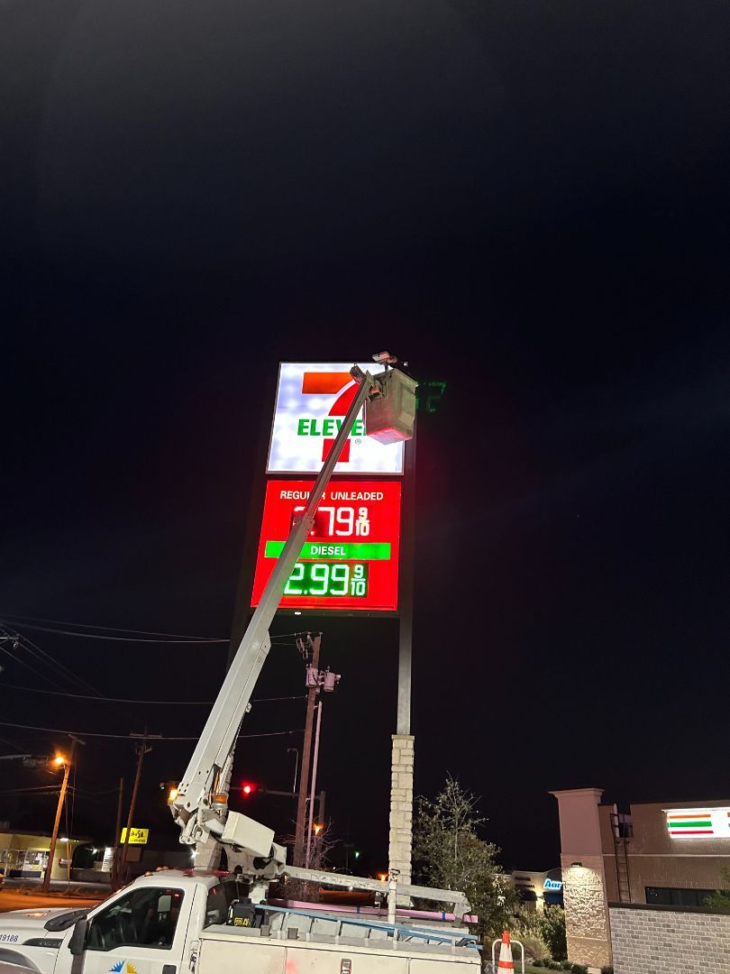 A man is working on a gas station sign at night.