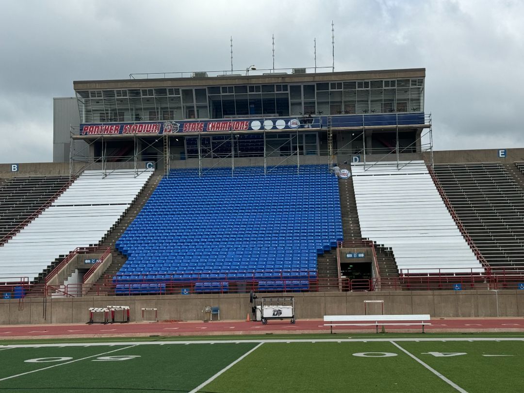 A stadium with blue and white seats and a large building in the background
