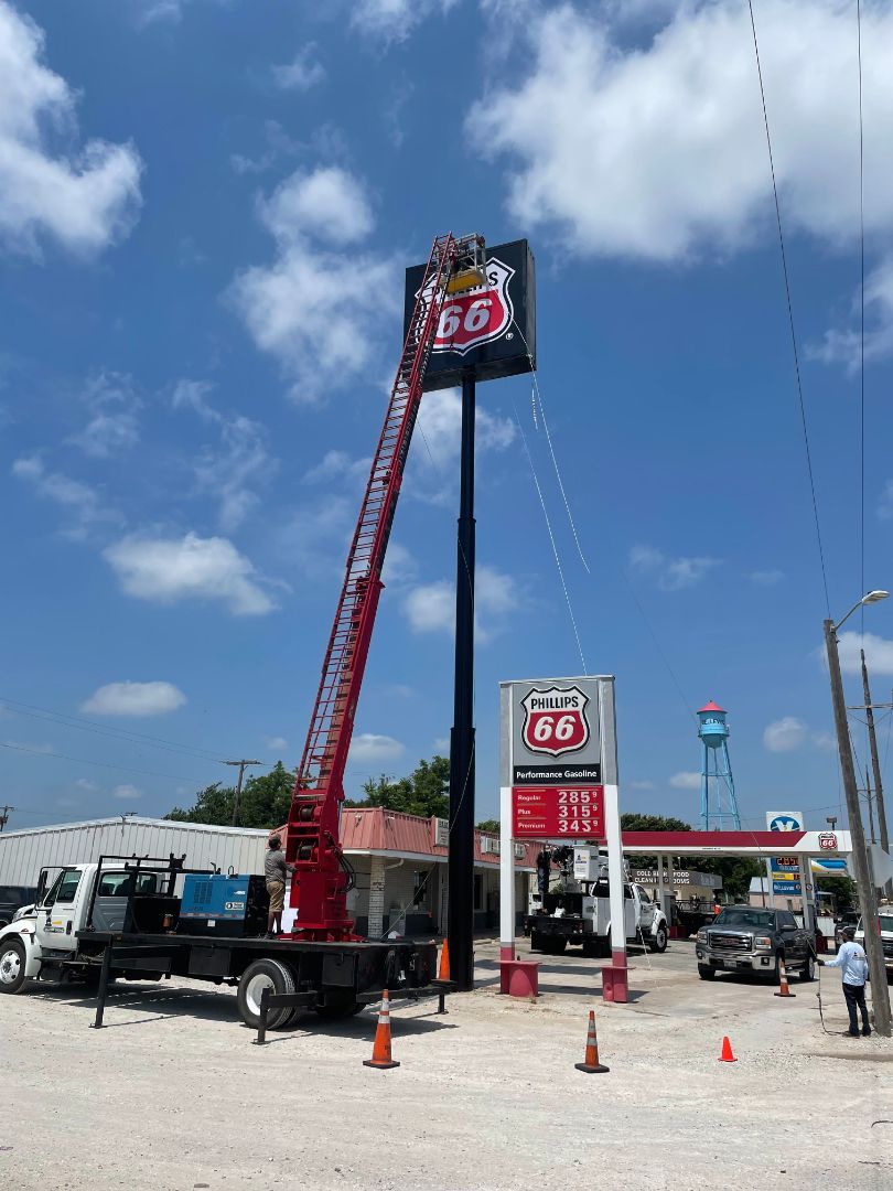 A crane is lifting a sign in front of a gas station.
