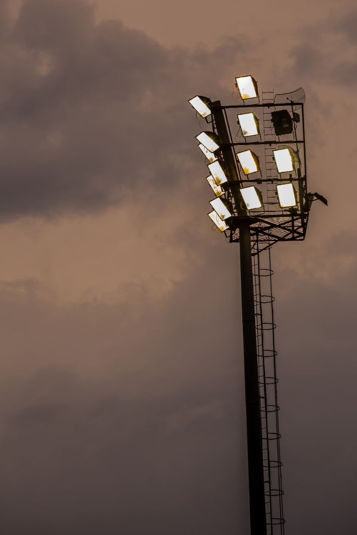 A stadium light is lit up against a cloudy sky