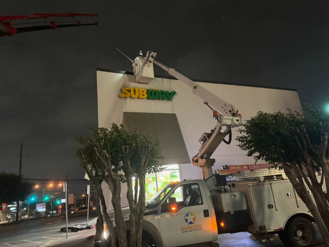 A subway sign is being installed on the side of a building at night.