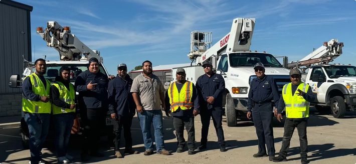 A group of construction workers are posing for a picture in front of trucks.