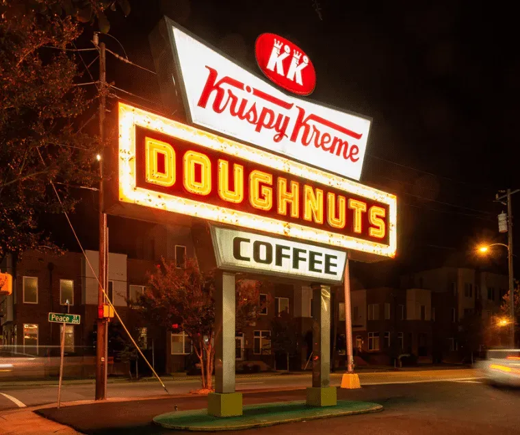 A krispy kreme doughnuts and coffee sign is lit up at night.