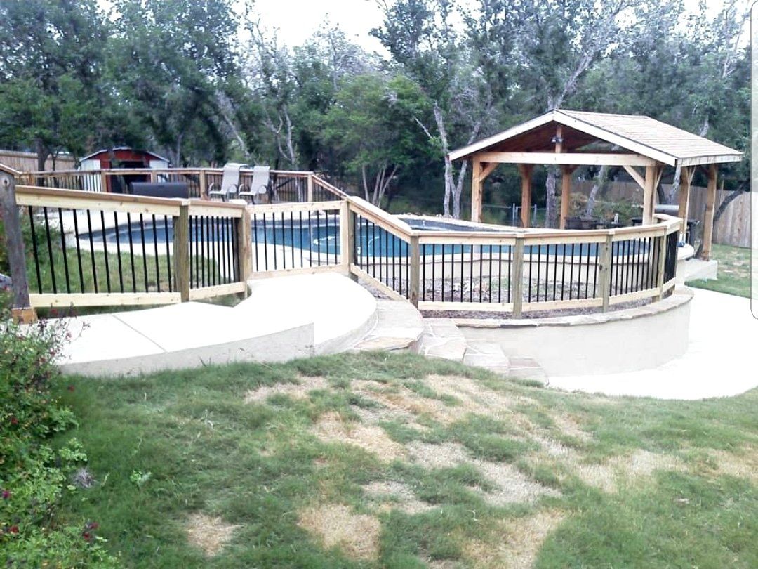 A wooden deck overlooking a swimming pool with a gazebo in the background.