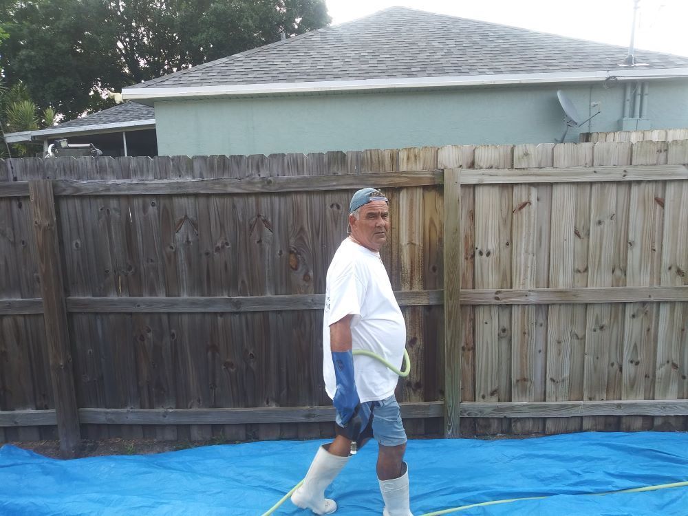 Image of a wood fence cleaning. You can see a fence that is getting washed. half of the fence is clean and the other half is stained. 