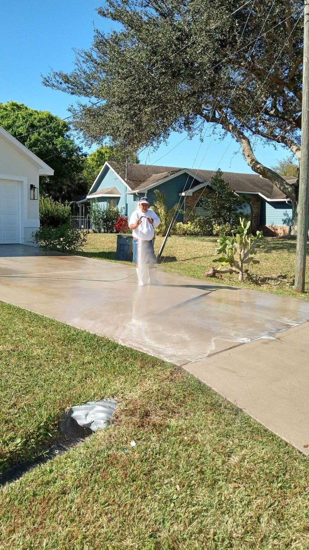 Picture showing a driveway getting pressure cleaned. You can see the owner of RNR Pressure Cleaning washing away stains from a driveway here in Palm City, FL.