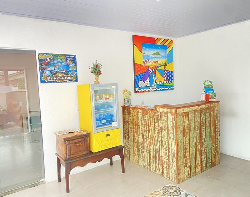 Uma área de recepção com um balcão rústico de madeira, um frigobar amarelo sobre um suporte de madeira e uma pintura abstrata colorida.