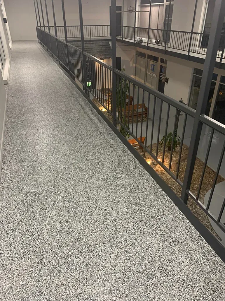 Indoor balcony walkway with black railing overlooking a lower atrium and storefronts