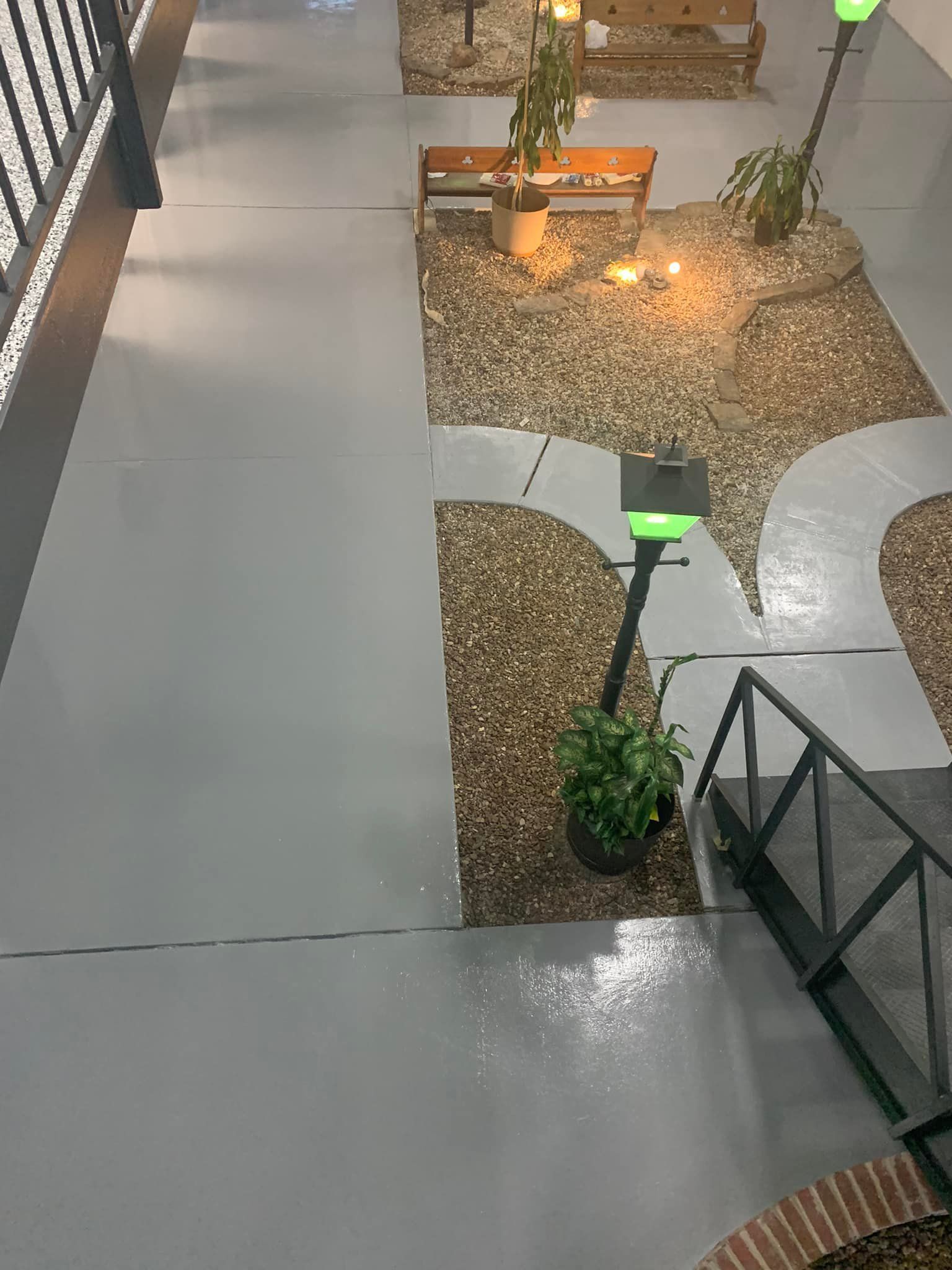 Indoor courtyard with gray floor, gravel planters, benches, and green lamp posts at night