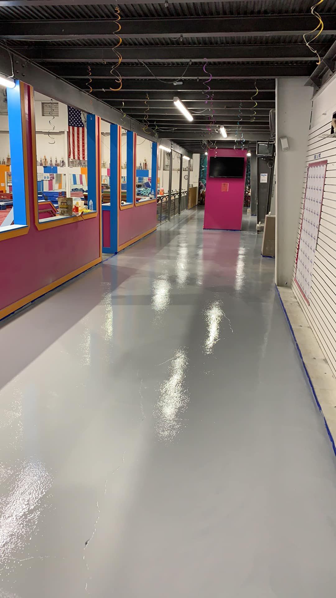 Empty hallway with glossy gray floor, colorful classroom walls on the left, and a pink door ahead.