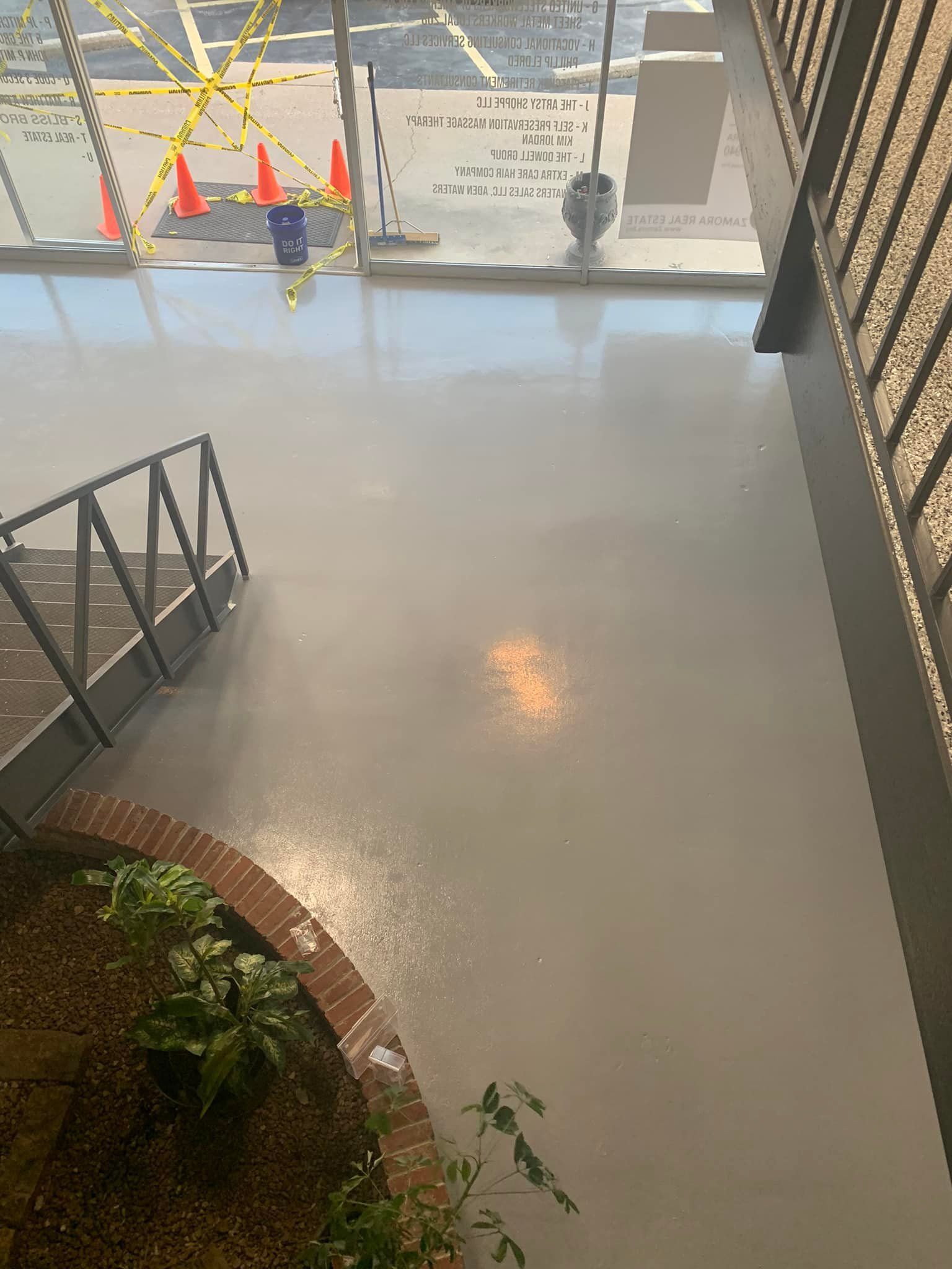 Flooded concrete floor in a covered outdoor area, with railing, plants, and light reflections.