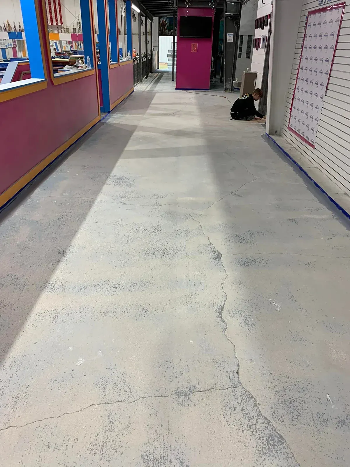 School hallway with scuffed white floor, colorful walls, and a magenta door at the end.