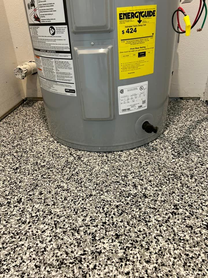Water heater in a basement corner on a speckled floor, with yellow energy guide labels on the tank.