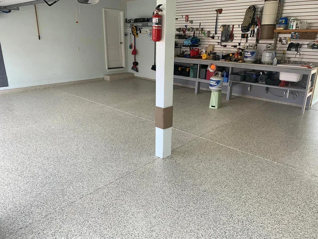 Spacious garage workshop with a speckled floor, central support post, and tools and supplies on shelves along the back wall