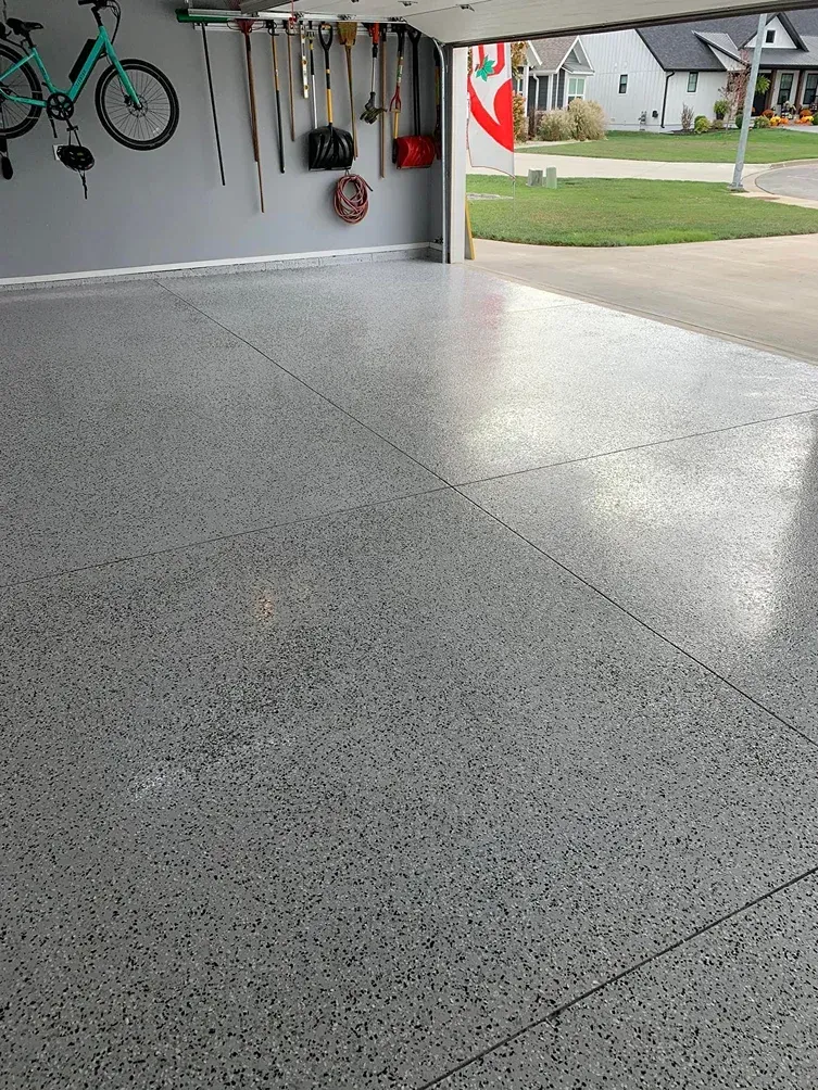 Garage interior with a speckled epoxy floor and open door to a suburban street
