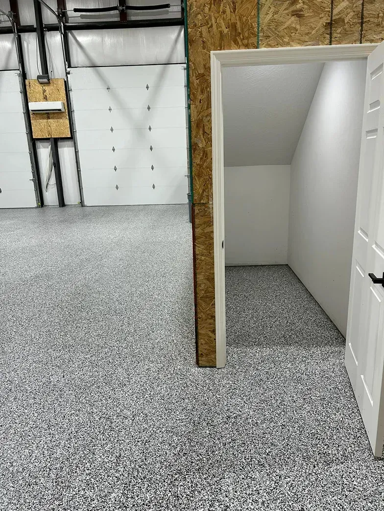 Indoor warehouse space with gray speckled floor, white doors, and an open small room